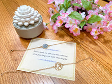 Load image into Gallery viewer, Globe golden bracelet and stone golden bracelet on top a Maya Angelou quote, flowers and a candle