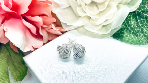 Knot earrings on top of white box and flowers as background