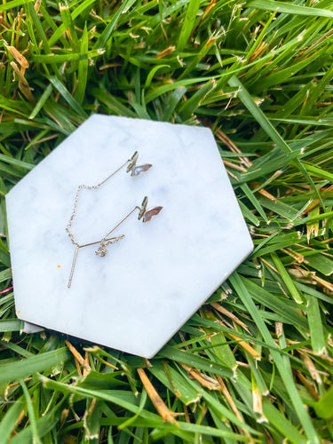 Butterfly dangle earrings on top of marble and grass